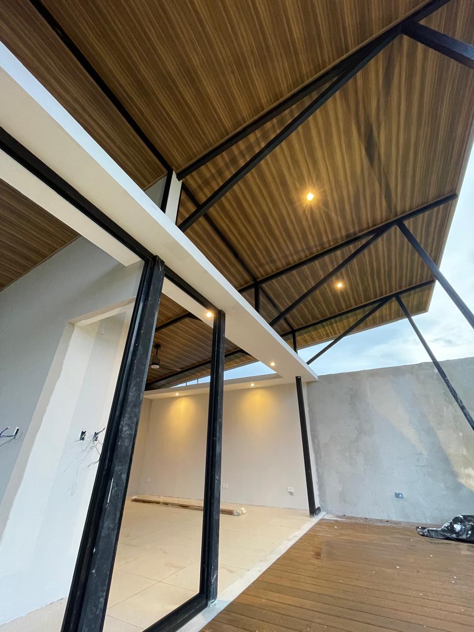 Construction detail — finished wood ceiling panels, black steel trusses, and interior downlights active on site